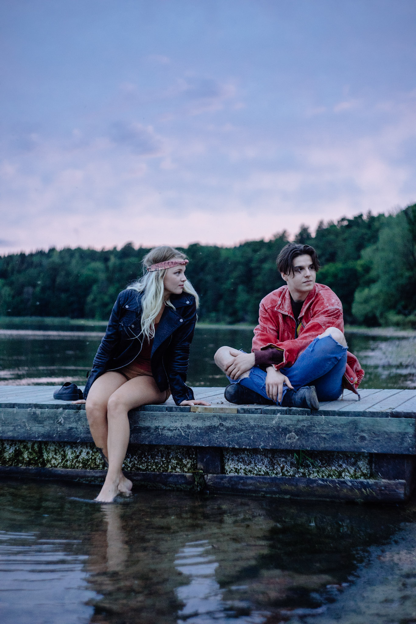 Två personer sitter på en brygga vid en sjö i kvällsljus.