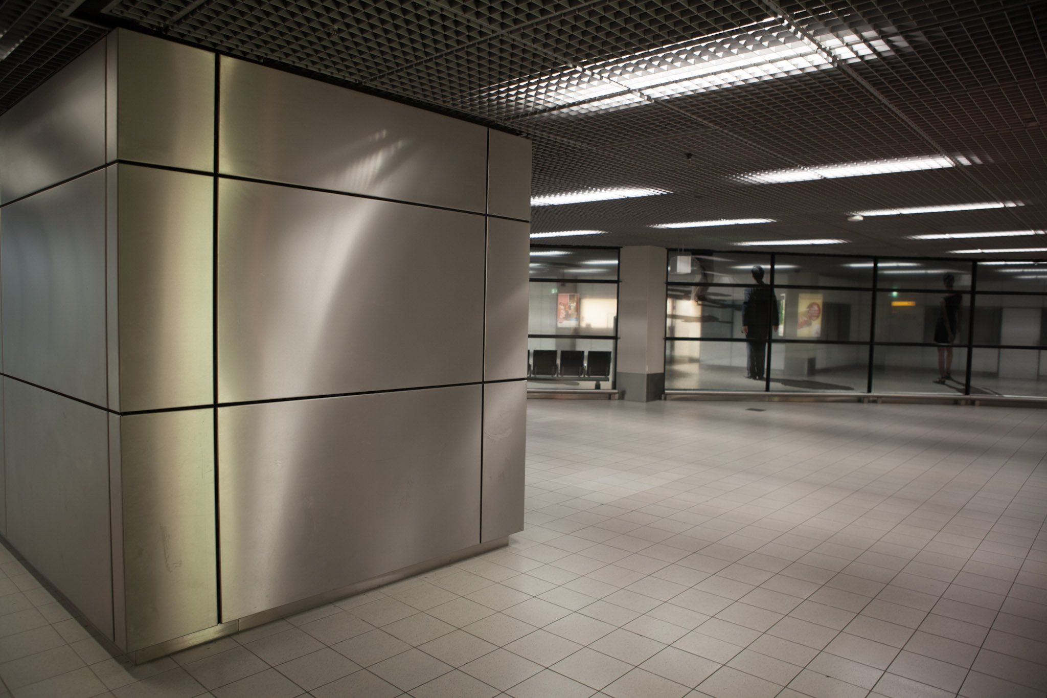 En tom passage med metallklädda pelare och lysrör i taket.