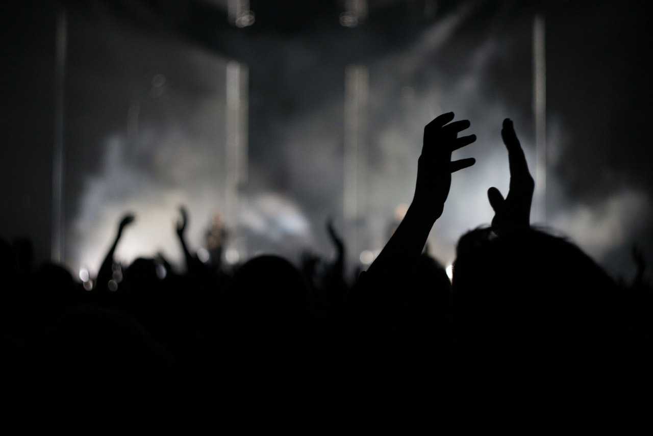 Uppsträckta händer i en mörk konsertpublik, fotograferade i svartvitt.