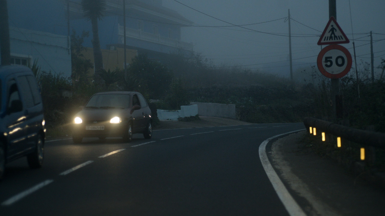 En bil med tända strålkastare möter kameran på en dimmig väg.