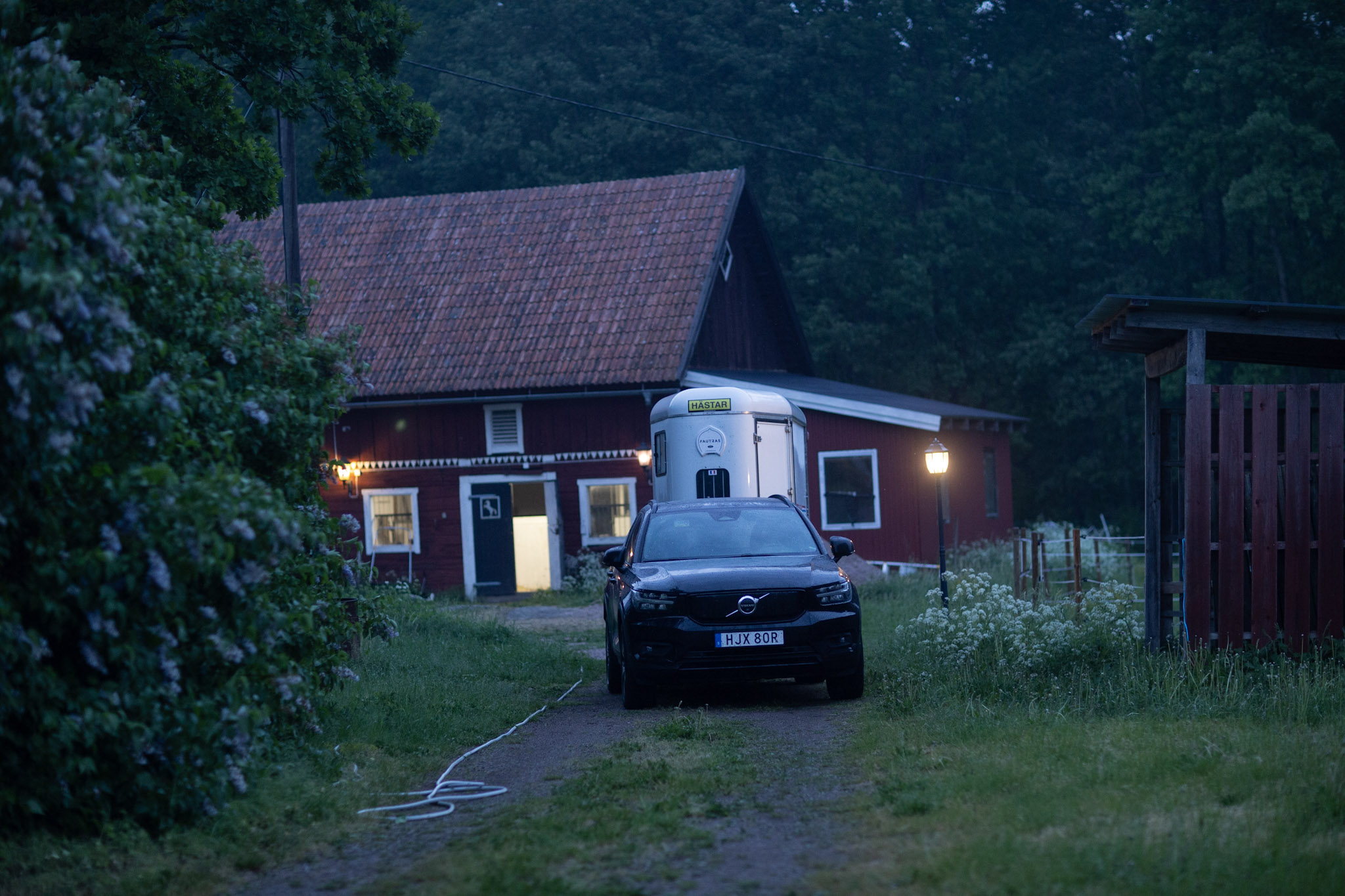 Ett rött hus med tända fönster och en parkerad bil i skymningen.