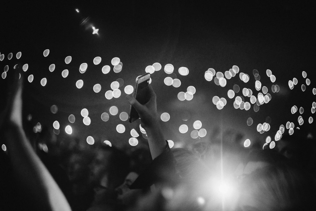 A black-and-white image of raised hands and phones amid out-of-focus points of light.