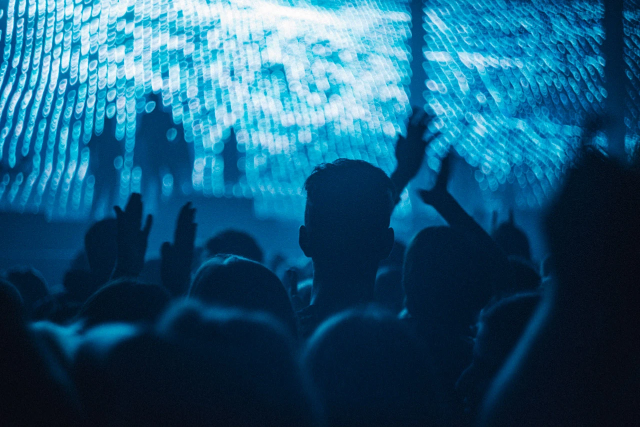 A concert audience and a raised hand silhouetted against blue stage light.