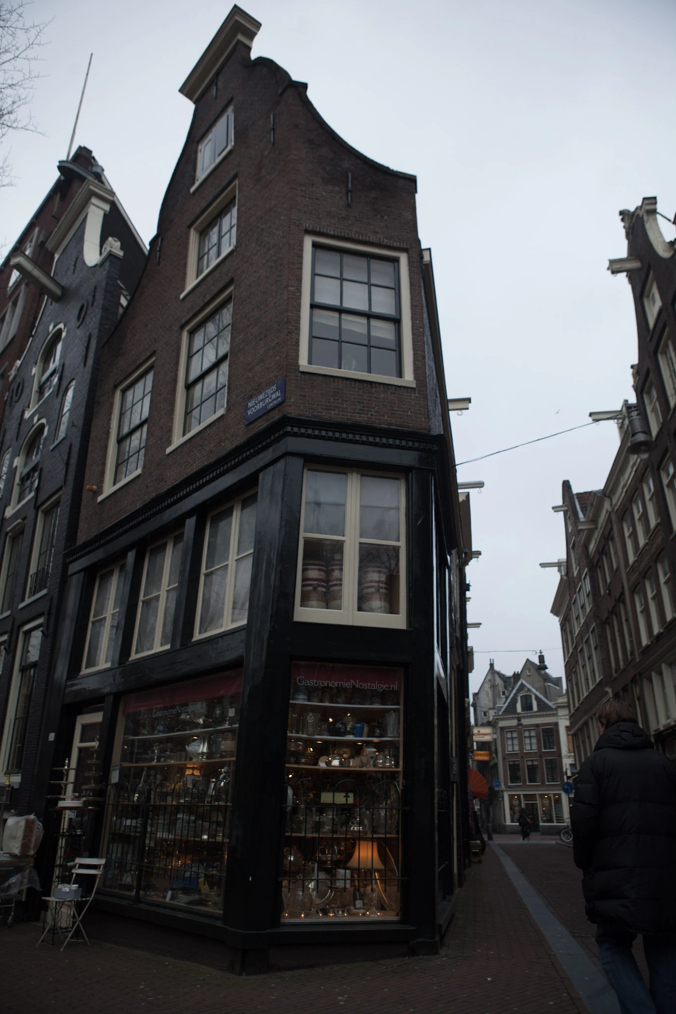A narrow dark brick house with large shop windows and tall gables beside an alley.