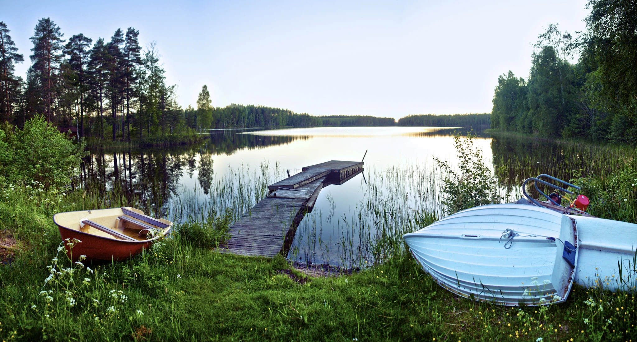 A tent and small boats sit beside still water surrounded by woodland.