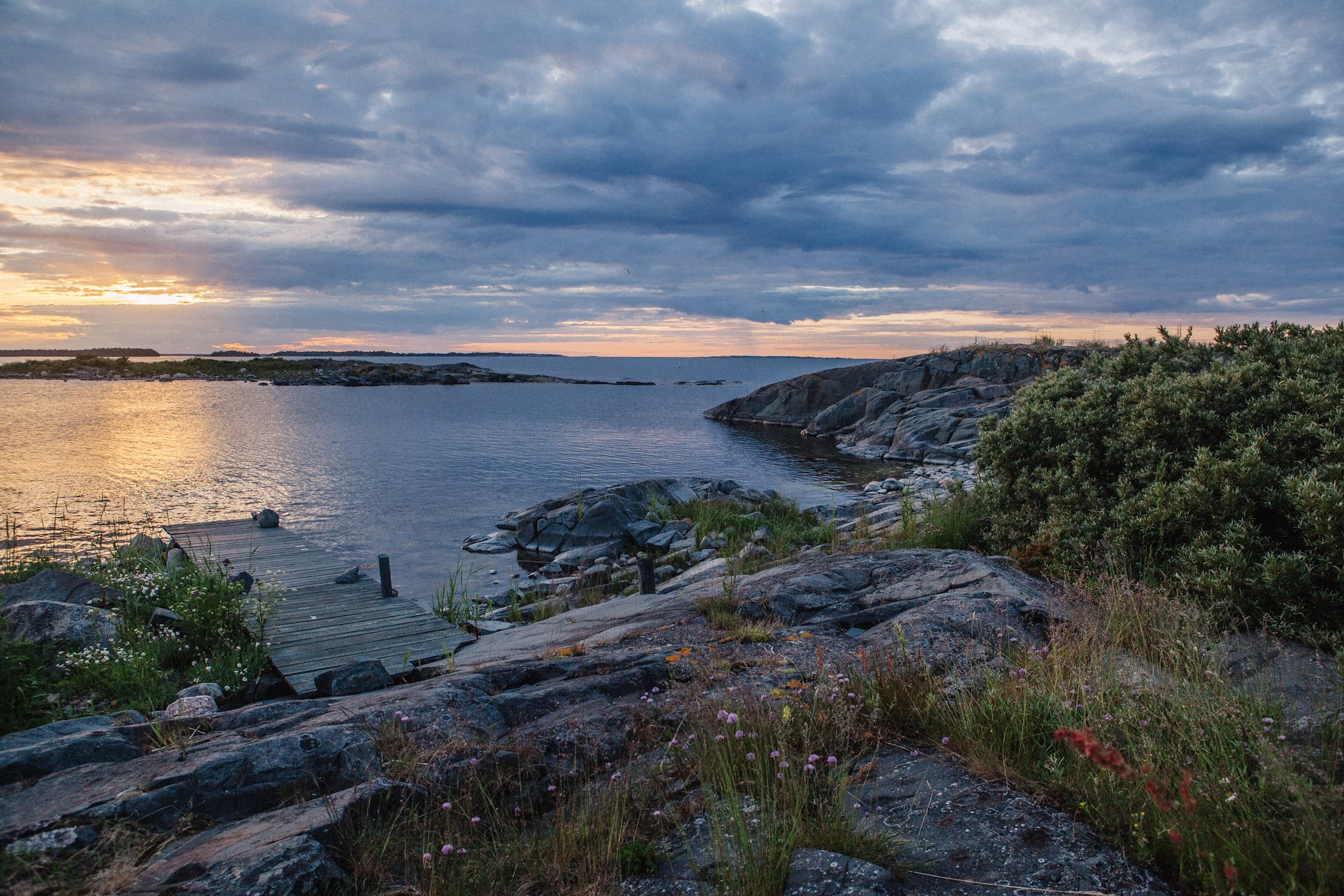 A small jetty and rocks surround a quiet bay beneath a broad cover of clouds.