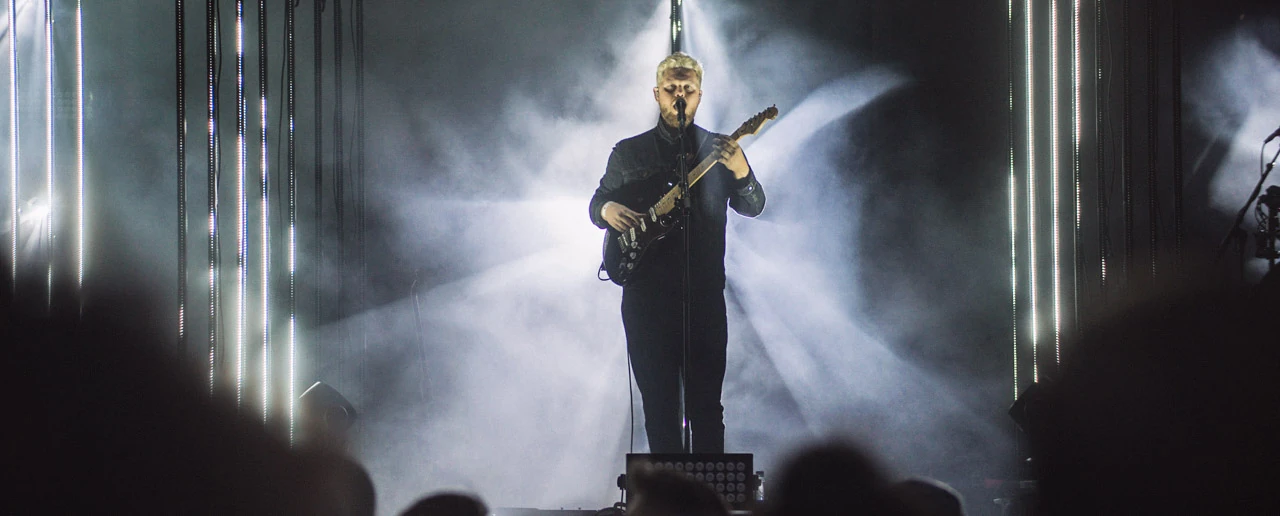 En ensam musiker i mörka kläder framför vita ljusstråk och rök.