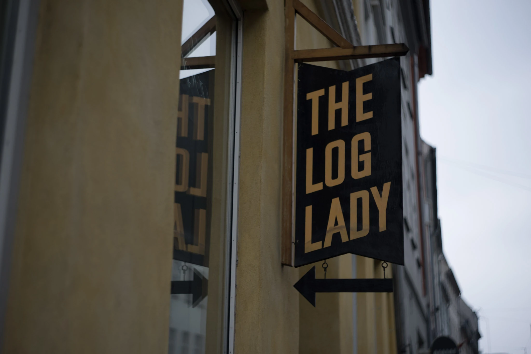A dark sign reading The Log Lady beside a building.