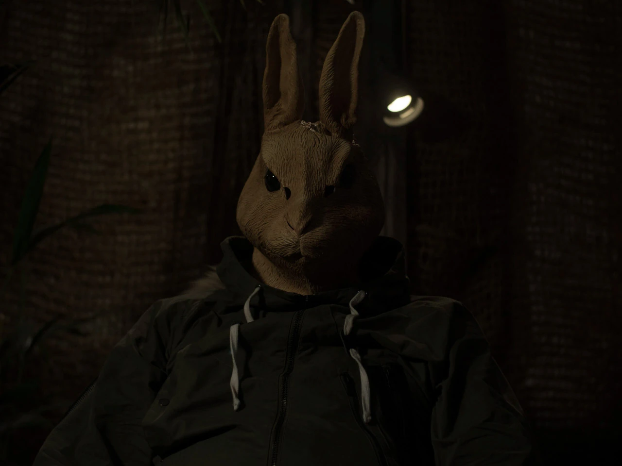 En person med kaninmask sitter i en mörk stol med ljus över masken.