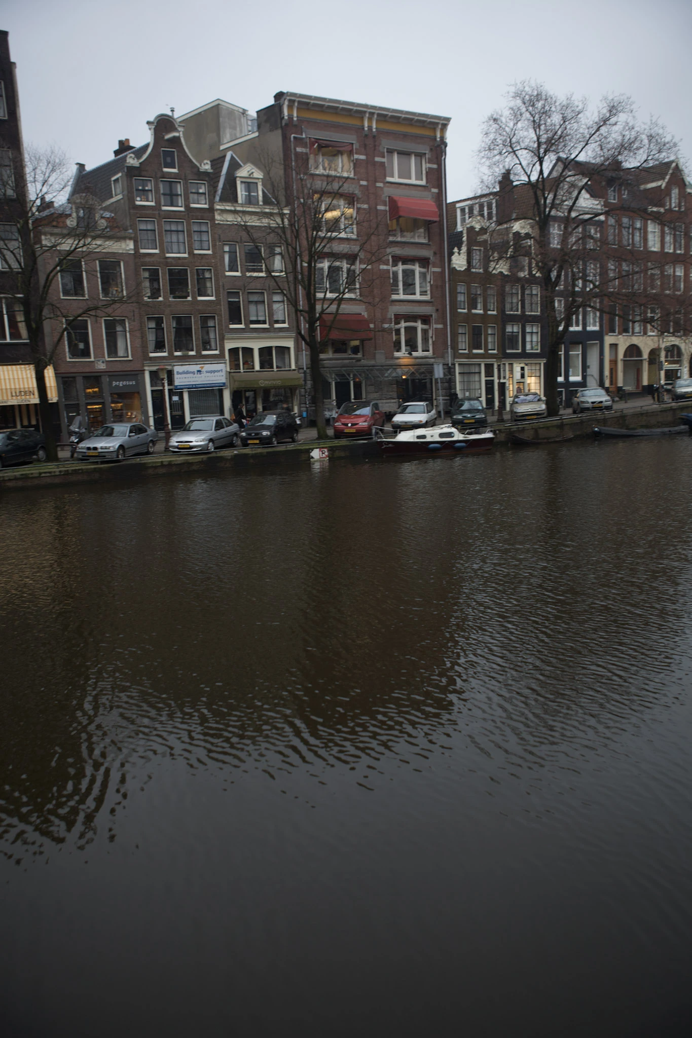 Narrow tall houses with varied gables beside dark canal water beneath a grey sky.