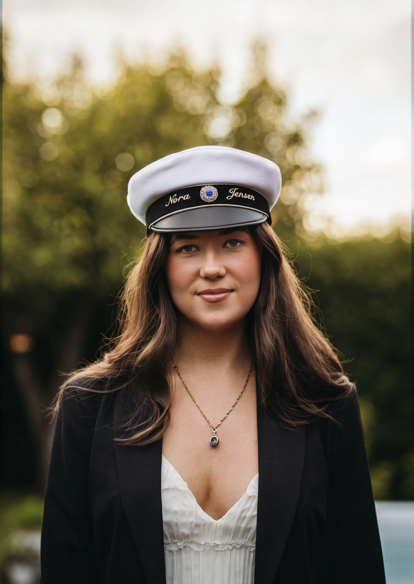 En ung kvinna i vit studentmössa porträtteras utomhus.
