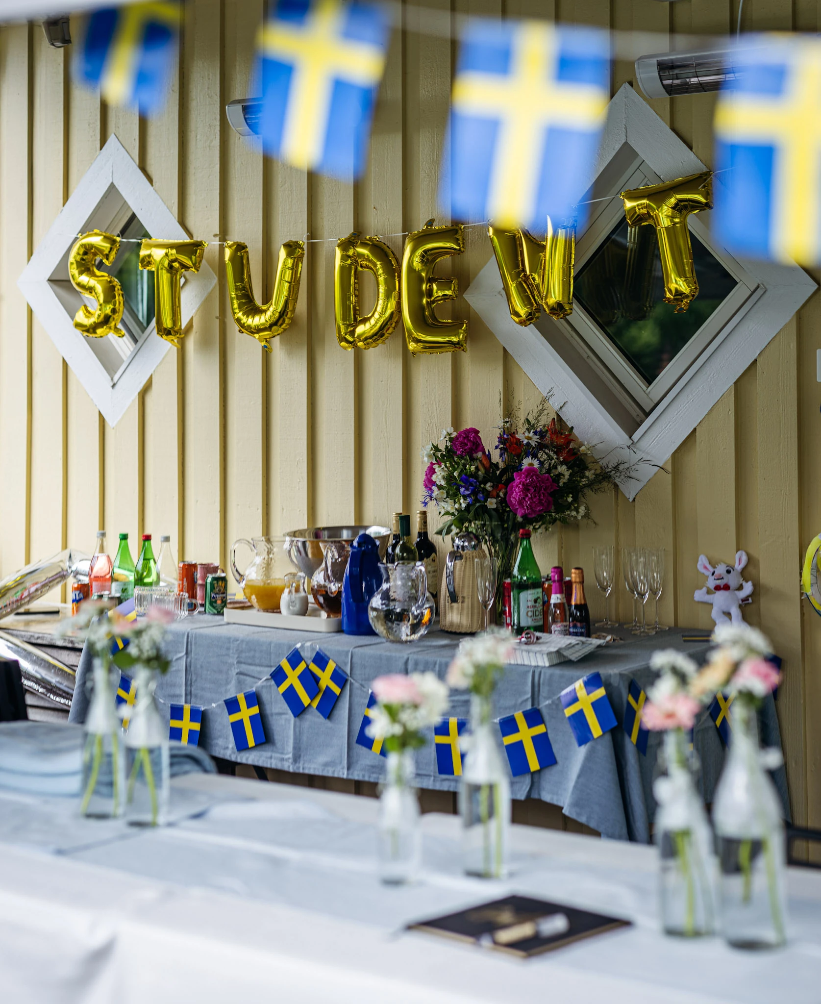 Gyllene bokstavsballonger och svenska flaggor vid studentfirandet.