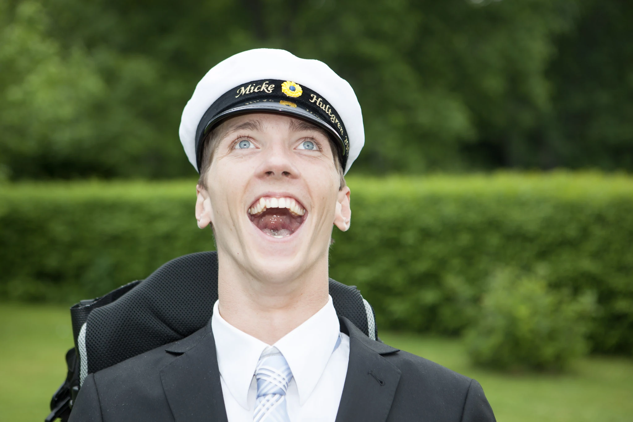 En ung man i studentmössa skrattar med ansiktet vänt uppåt.