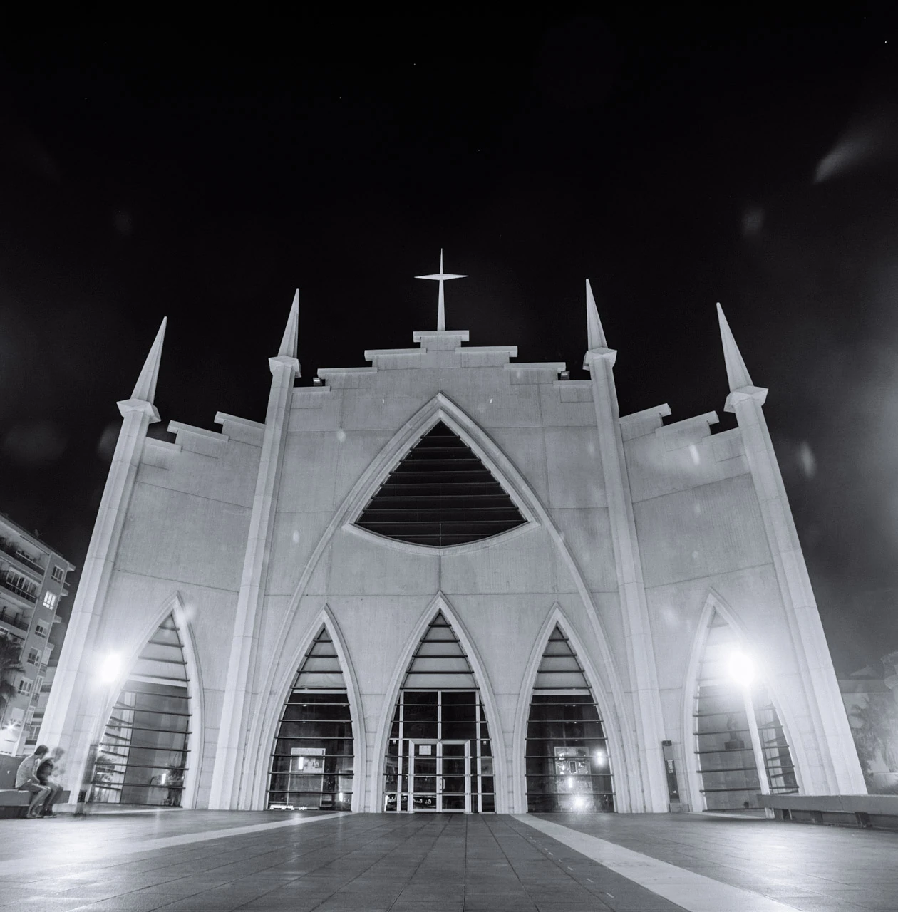 An illuminated church facade with pointed arches seen from below against a black sky.