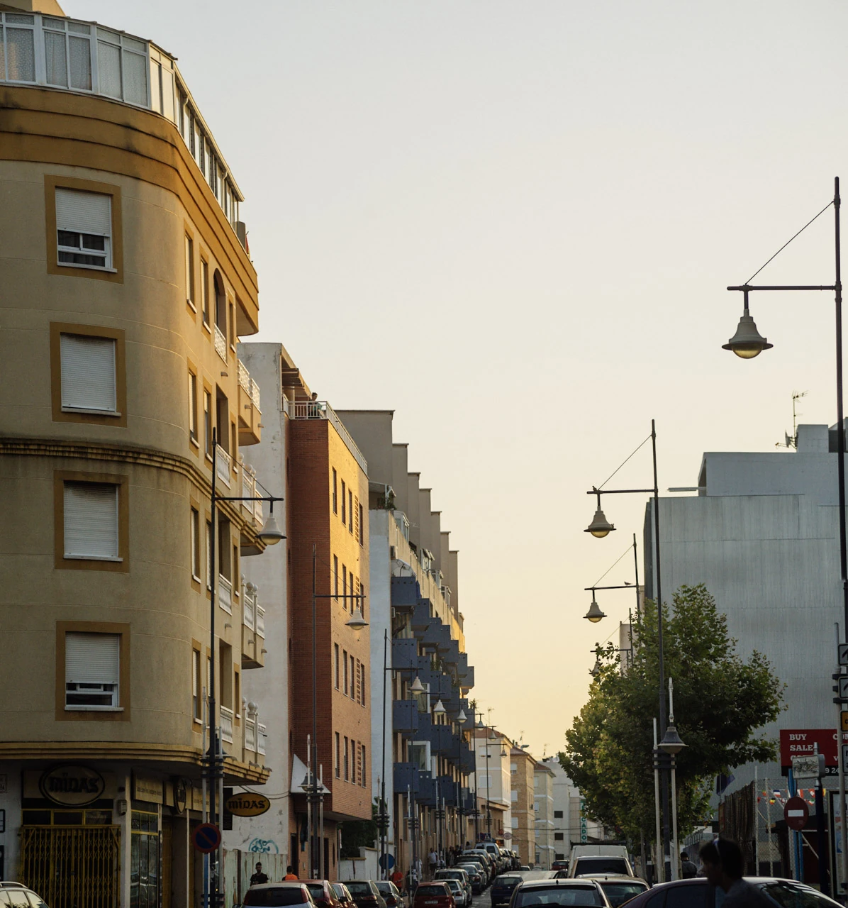 Tall buildings and street lamps along a street in evening light.