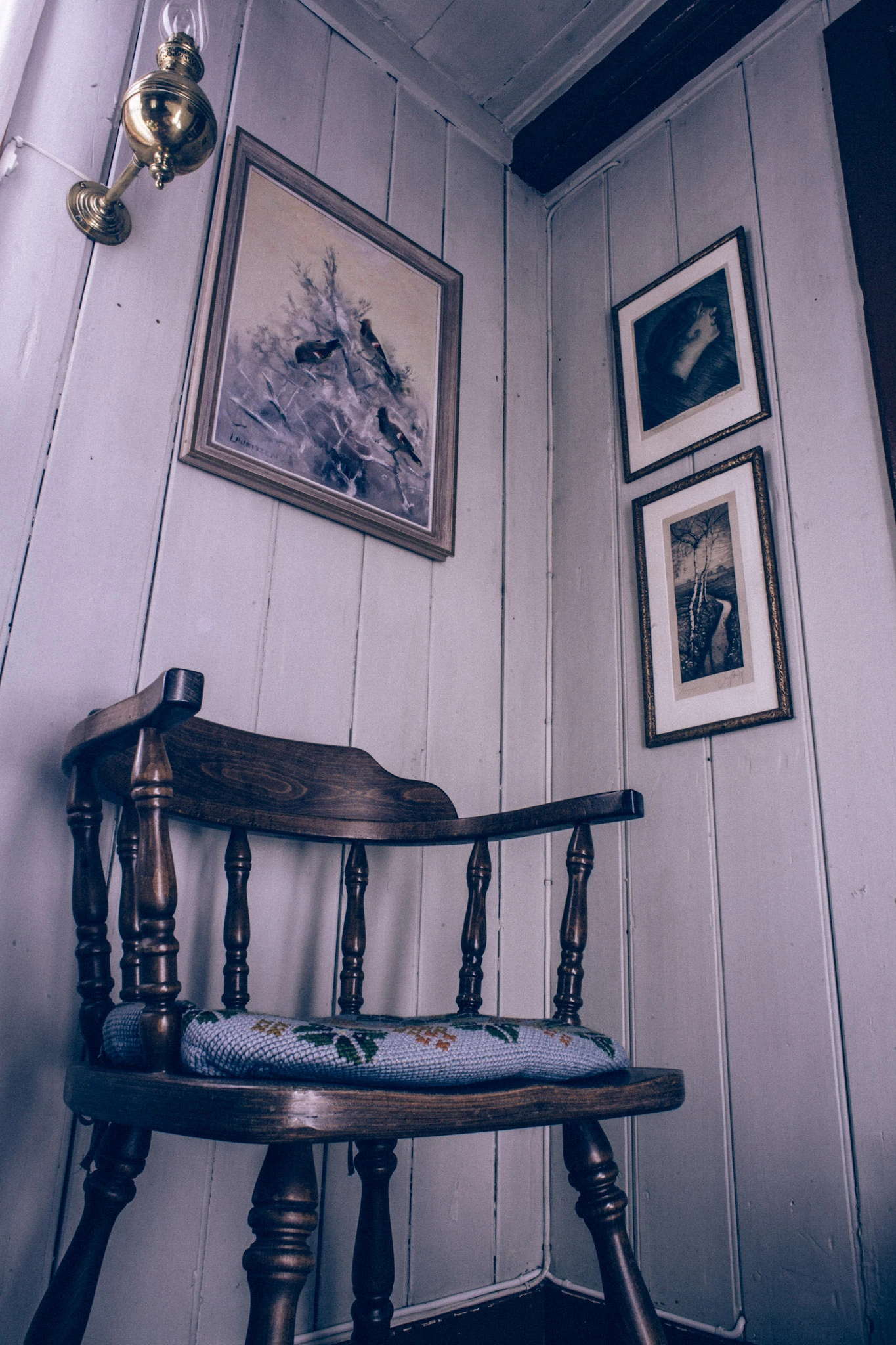 En mörk trästol i ett hörn med ljusa träväggar och flera inramade bilder.