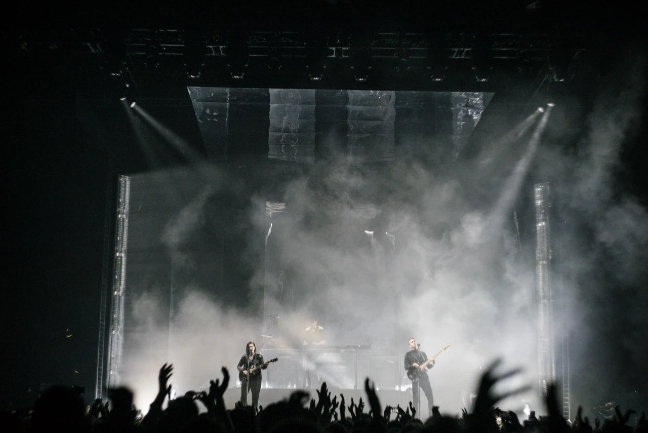 Raised hands in front of musicians and white haze on a dark stage.