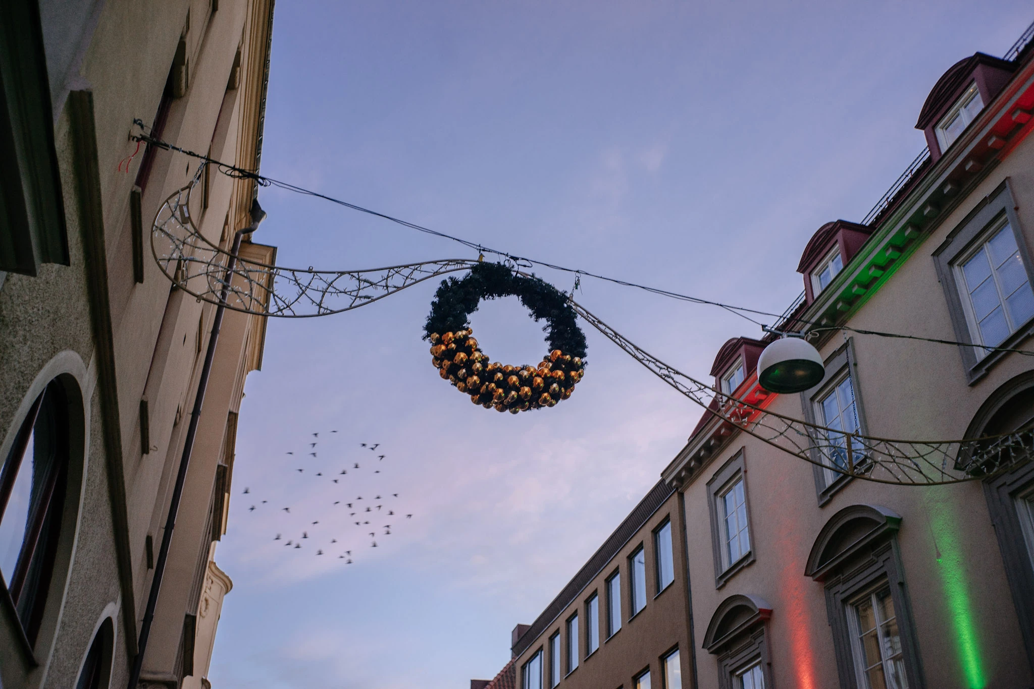 A wreath hanging between buildings against a blue dusk sky.