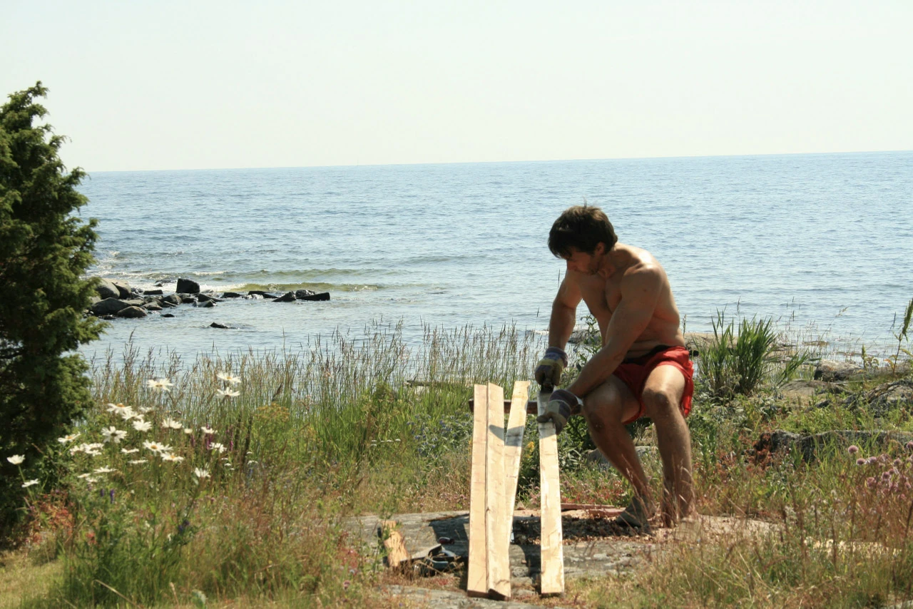 En person arbetar med trä på en gräsplätt vid havet.