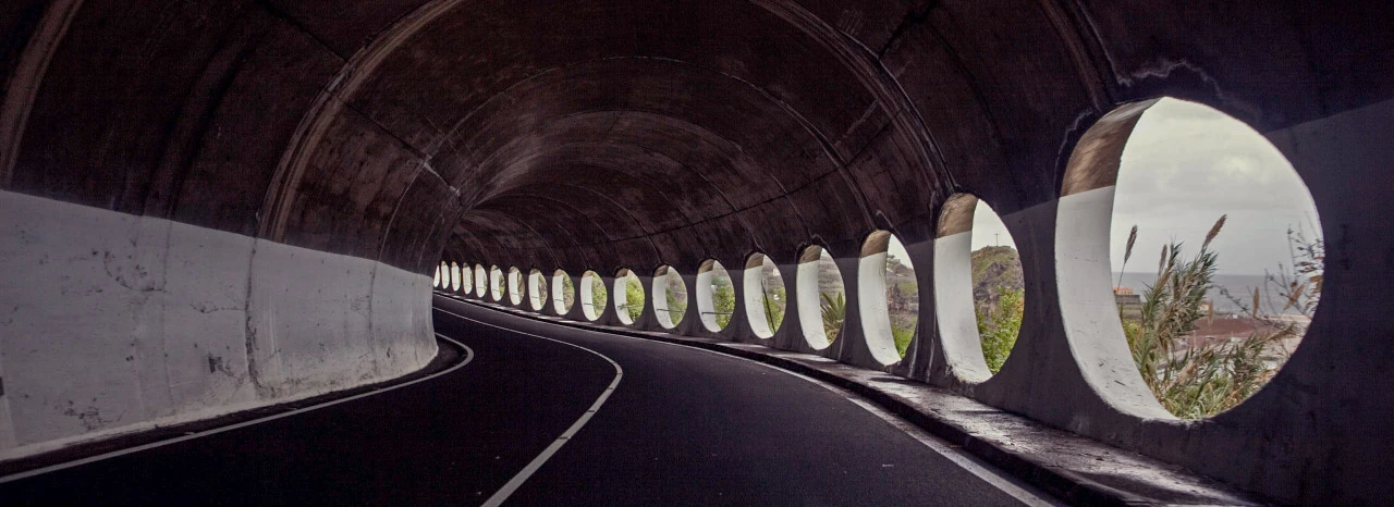 En väg svänger genom en mörk tunnel med runda ljusöppningar.