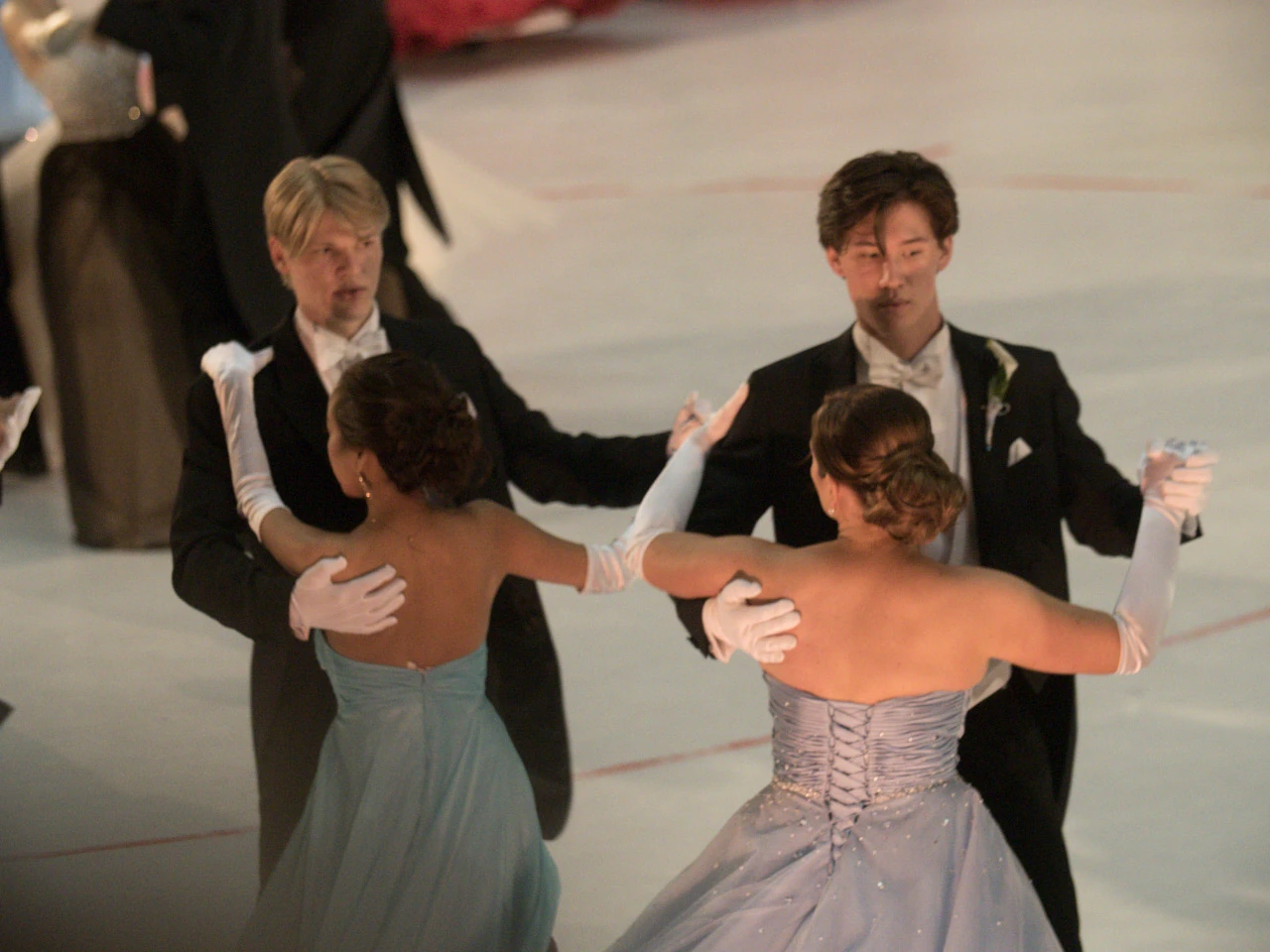 Festklädda par dansar på ett ljust arenagolv.