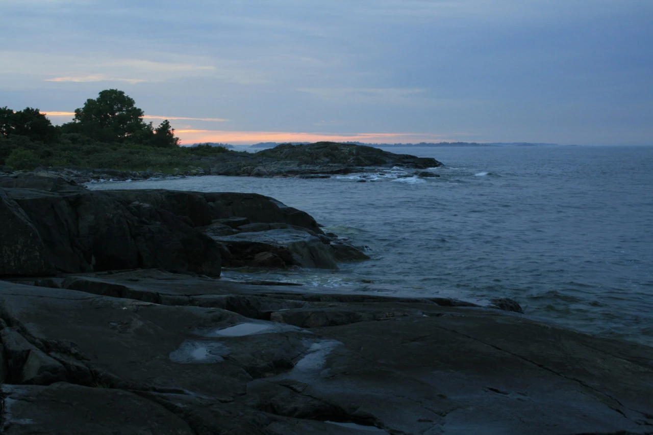 Dark rocks and open sea beneath a blue sky with a thin warm band on the horizon.