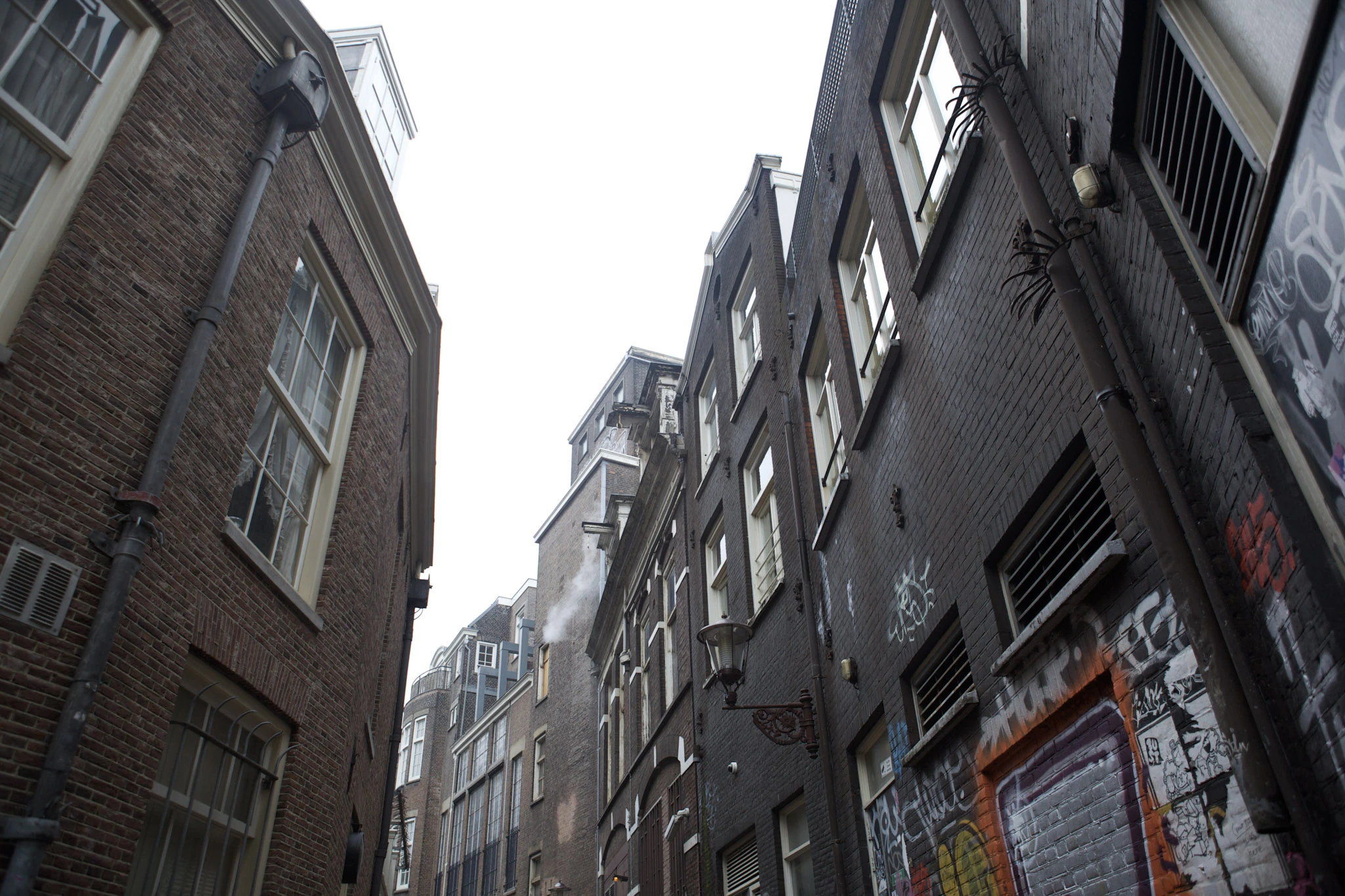 Tall narrow brick houses and a streetlamp seen from a low viewpoint in an alley.