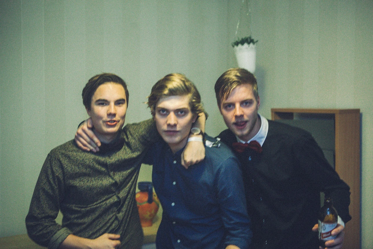Tre män lutar sig samman framför kameran på en fest.
