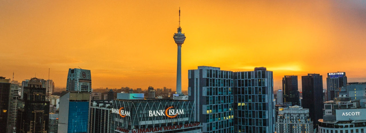 A city skyline with a tall tower against an orange sky.
