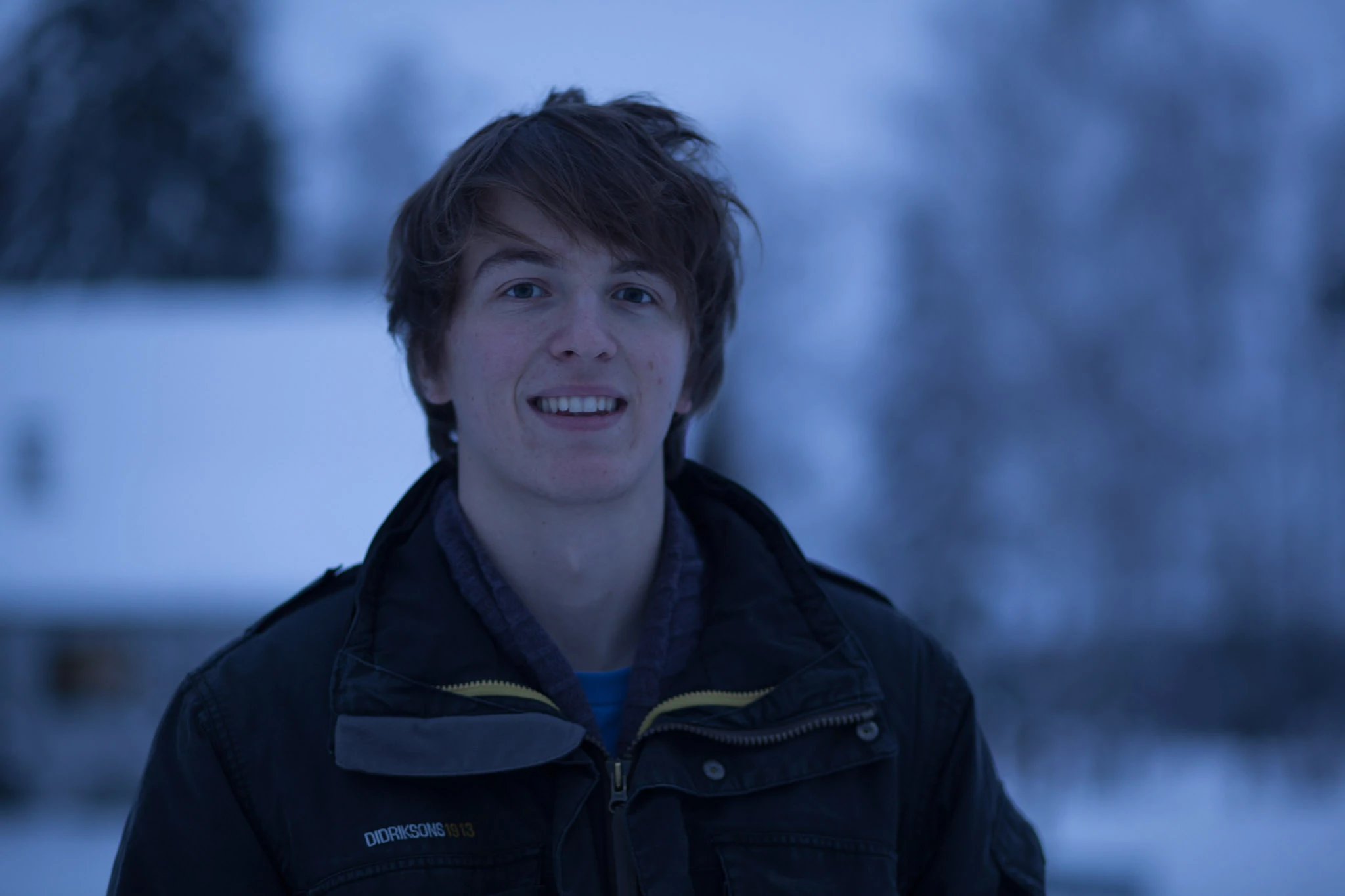 En ung man i mörk jacka porträtteras mot en snöig blå skymning.