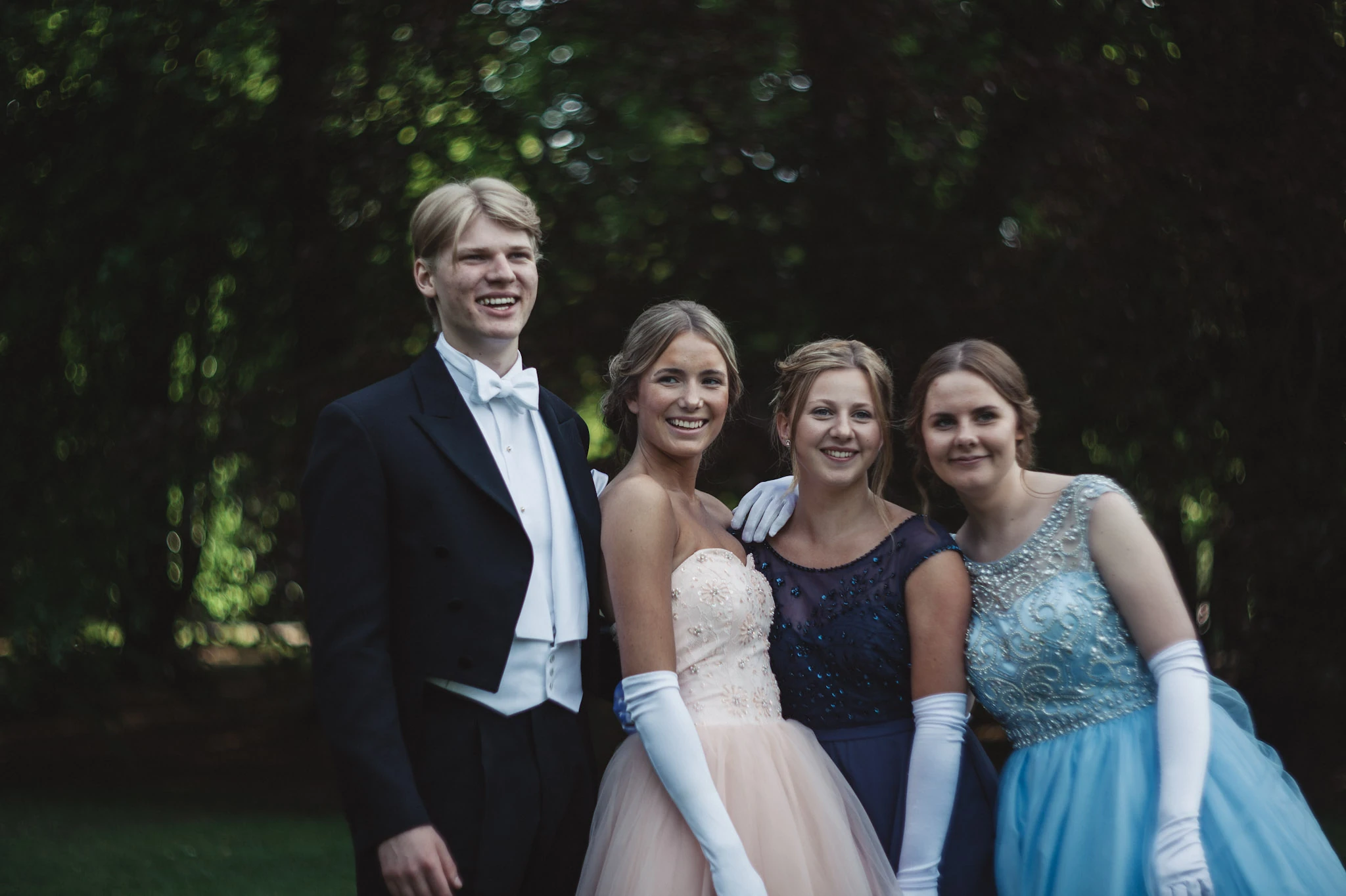 Fyra balgäster står nära varandra framför mörk grönska.