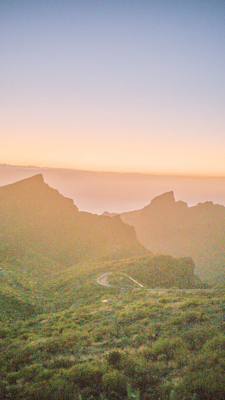 Green mountainsides and pointed ridges below a soft orange evening sky.