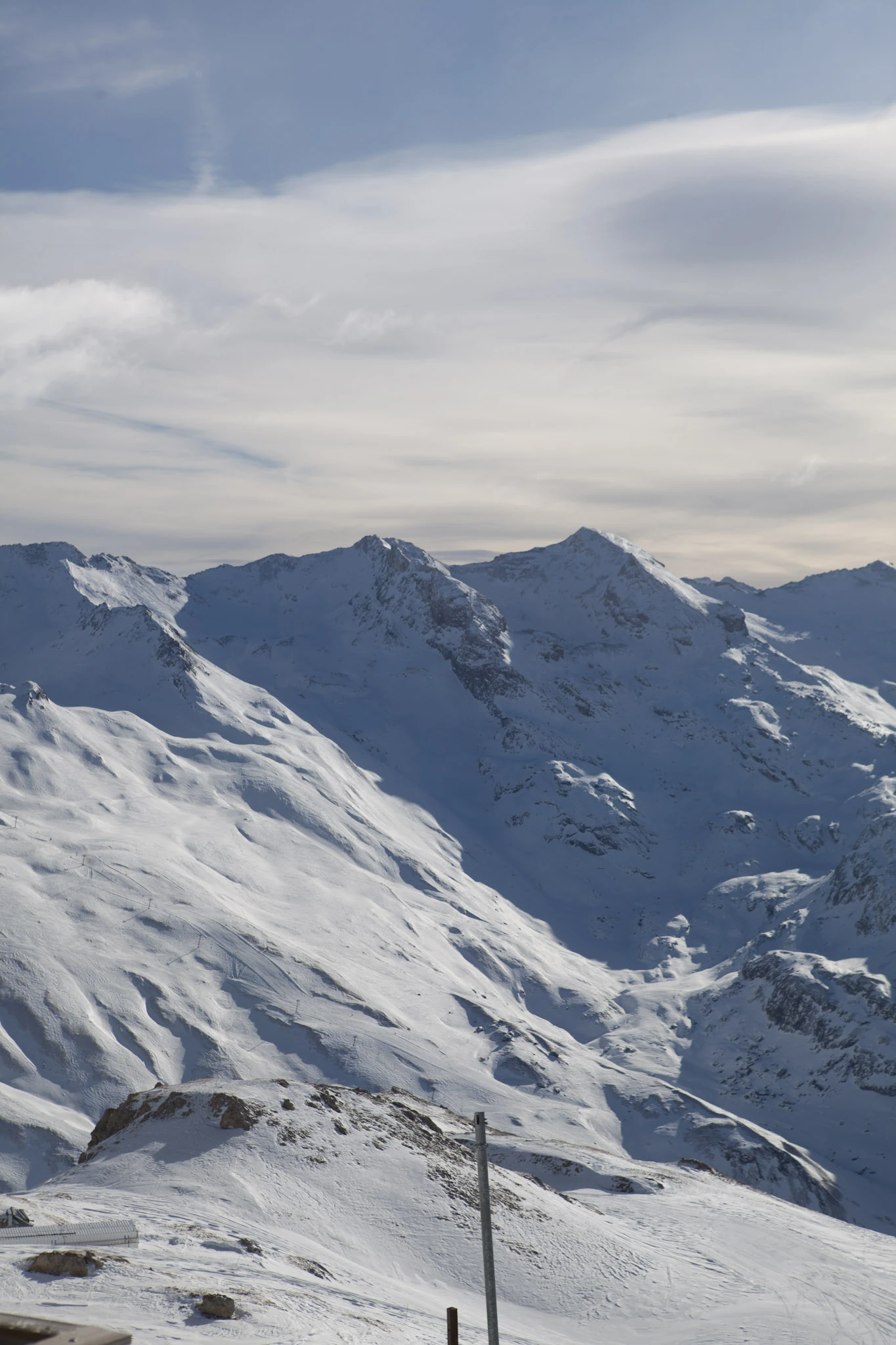 Snow-covered mountain ridges beneath soft clouds and blue sky.