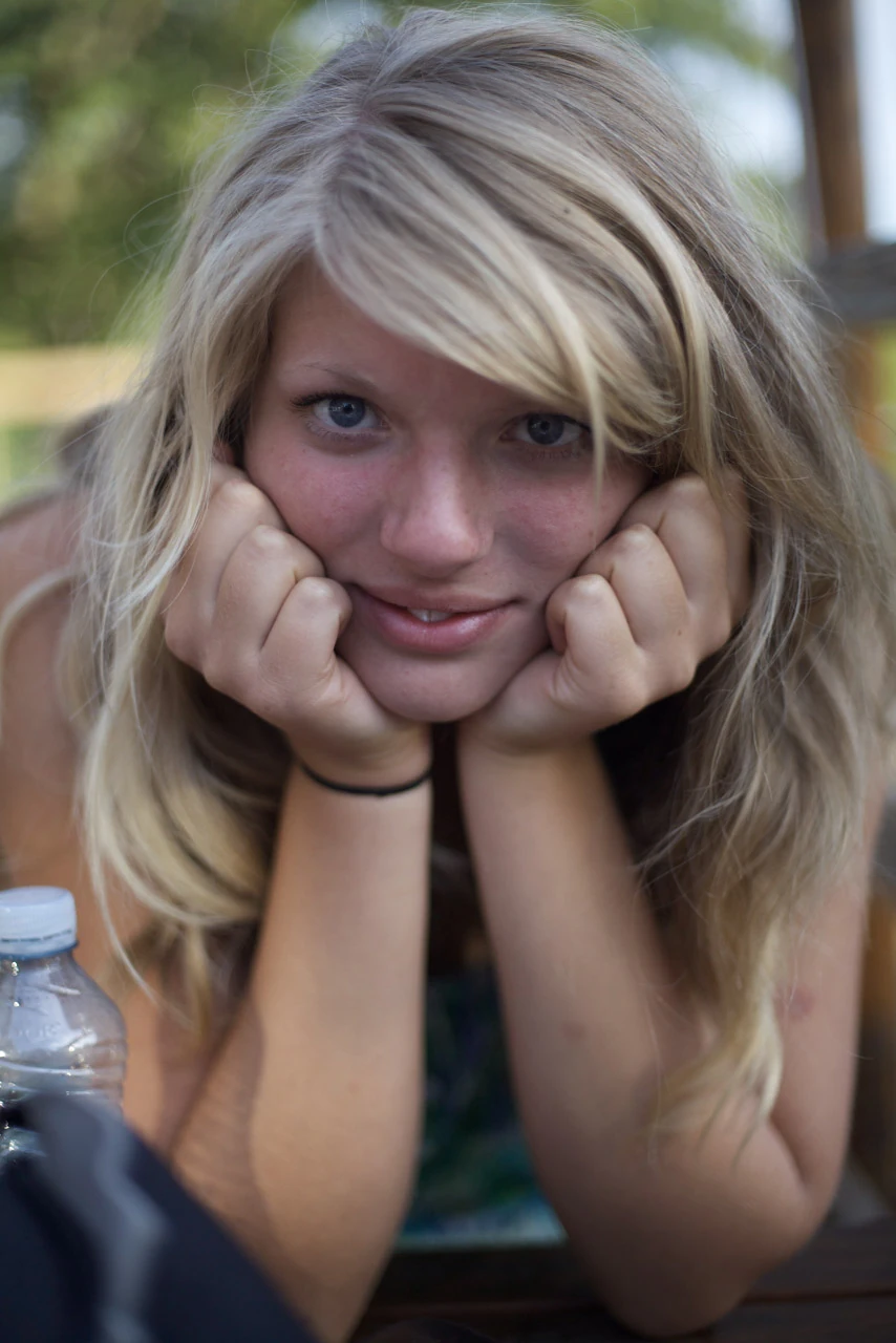 En blond kvinna vilar hakan i händerna framför mjuk grönska.
