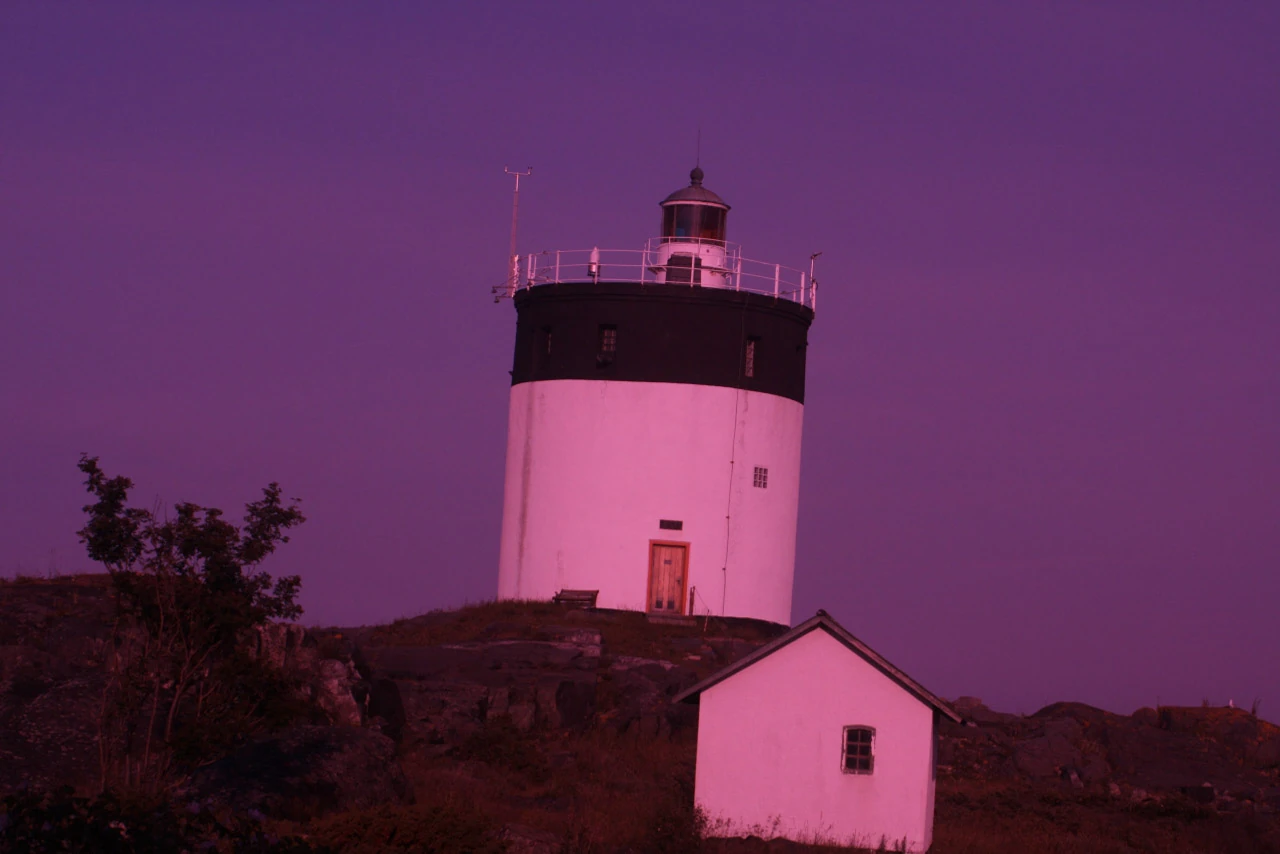 A white lighthouse with a black band against a vivid pink and purple sky.