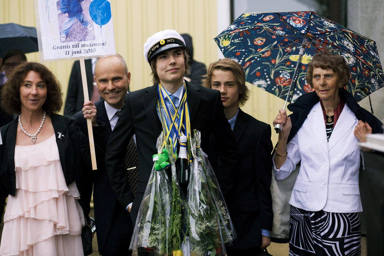 En student och familj står tillsammans under paraplyer.