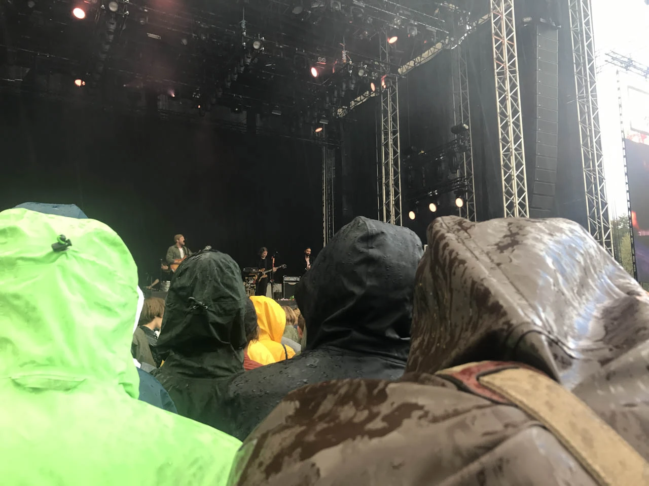 Festival visitors in rain ponchos stand in front of a dark stage.