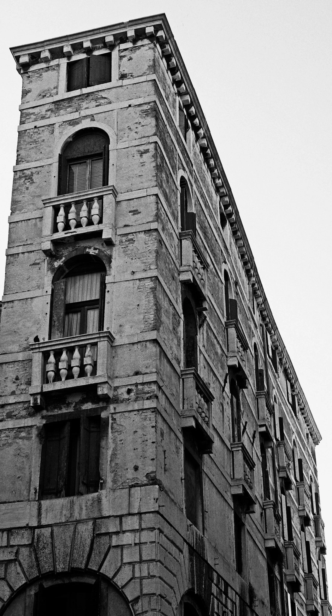 A black-and-white view up a narrow tall facade with balconies, arched windows and decorative stonework.