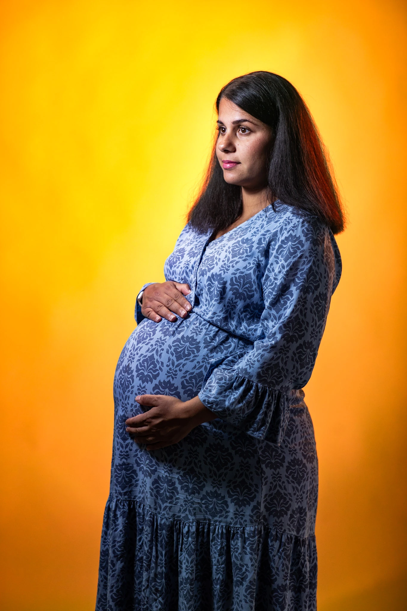 En gravid kvinna i mönstrad klänning mot en orange studiofond.