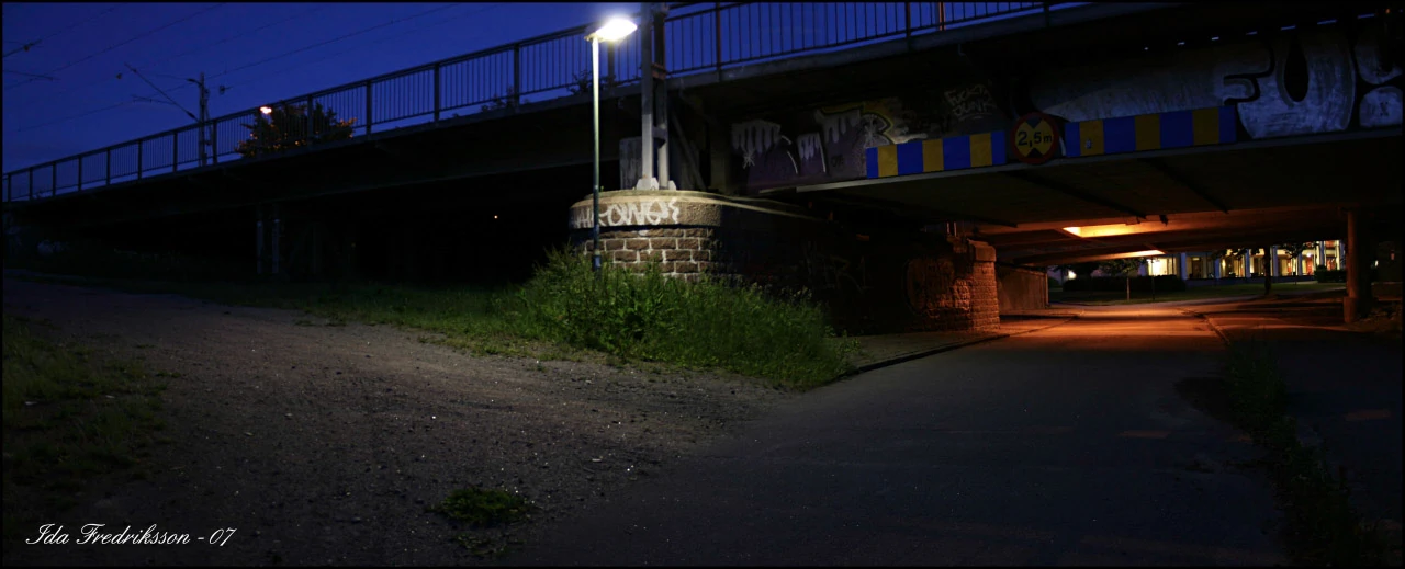 A path beneath a bridge with a blue evening sky and warm light from the underpass.