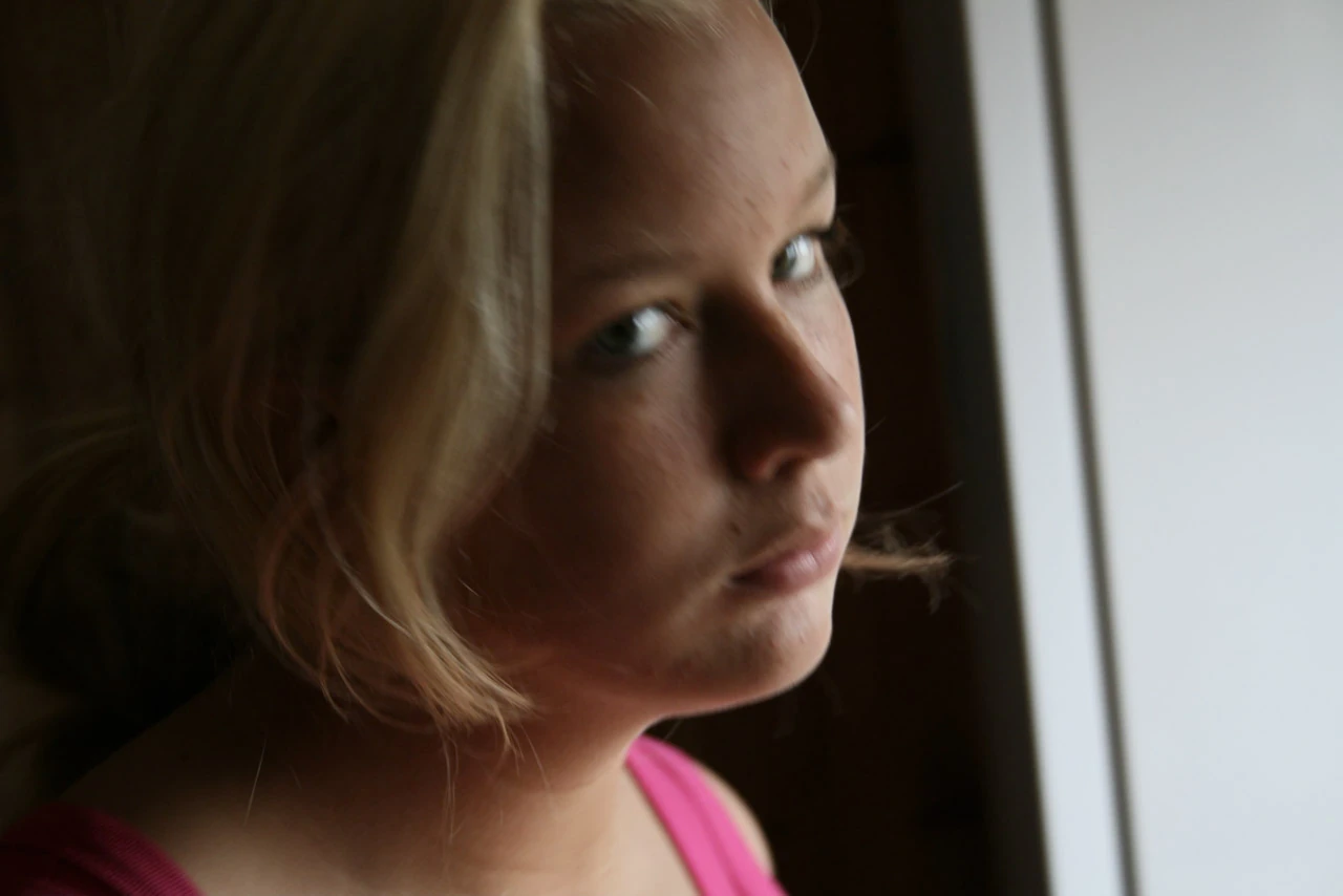En ung kvinna vänder ansiktet mot kameran i mjukt fönsterljus.