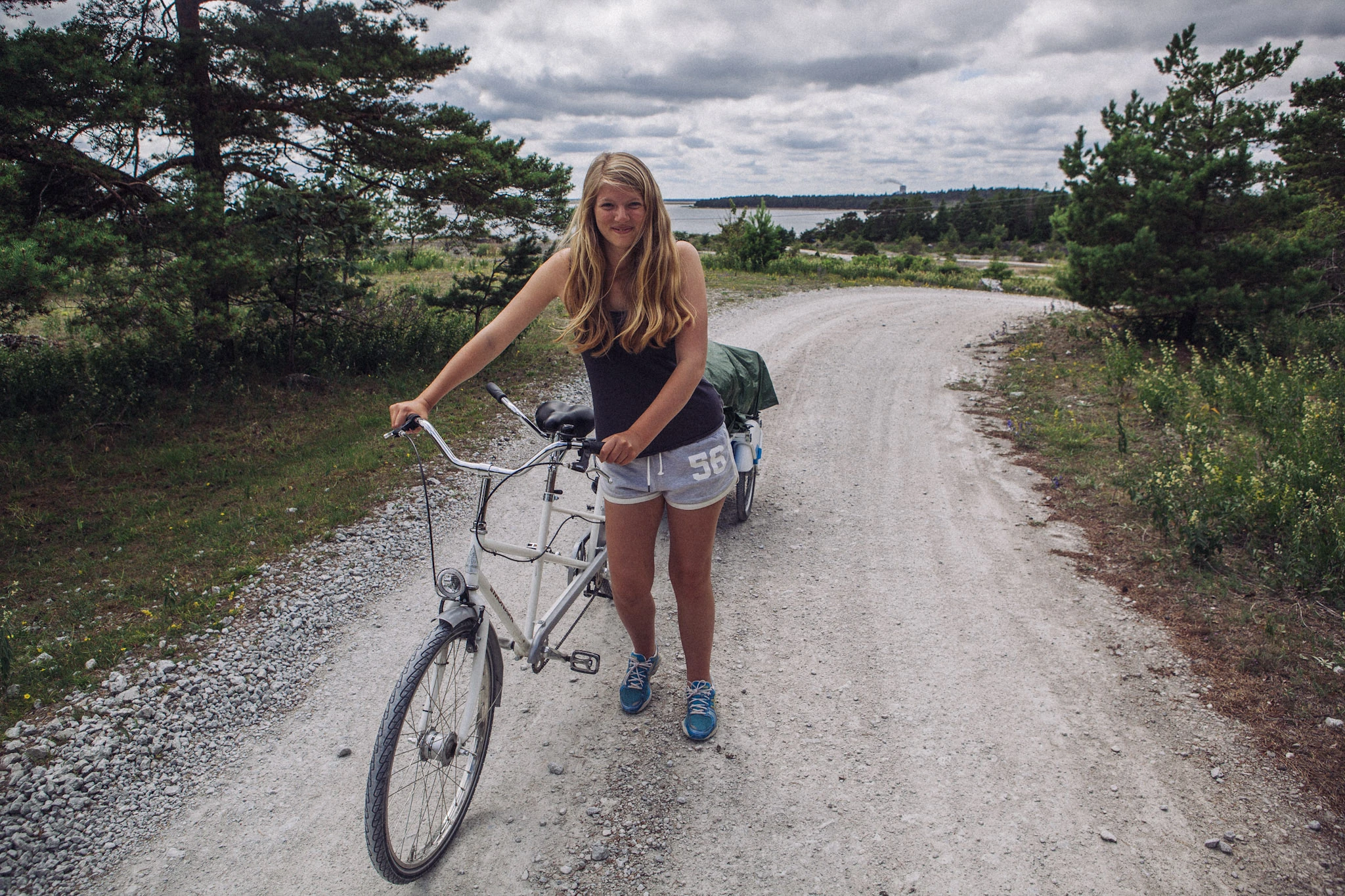 A person pushes a bicycle along a winding gravel road.