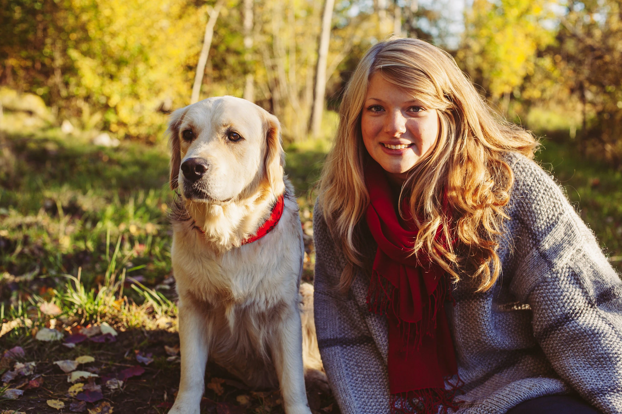 En kvinna med röd halsduk sitter med en hund i gyllene höstskog.