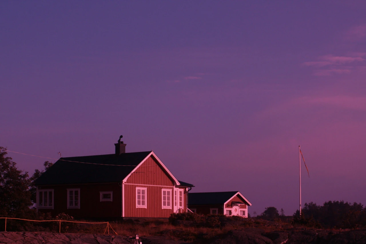 A red wooden house and a smaller cottage beneath a purple evening sky.