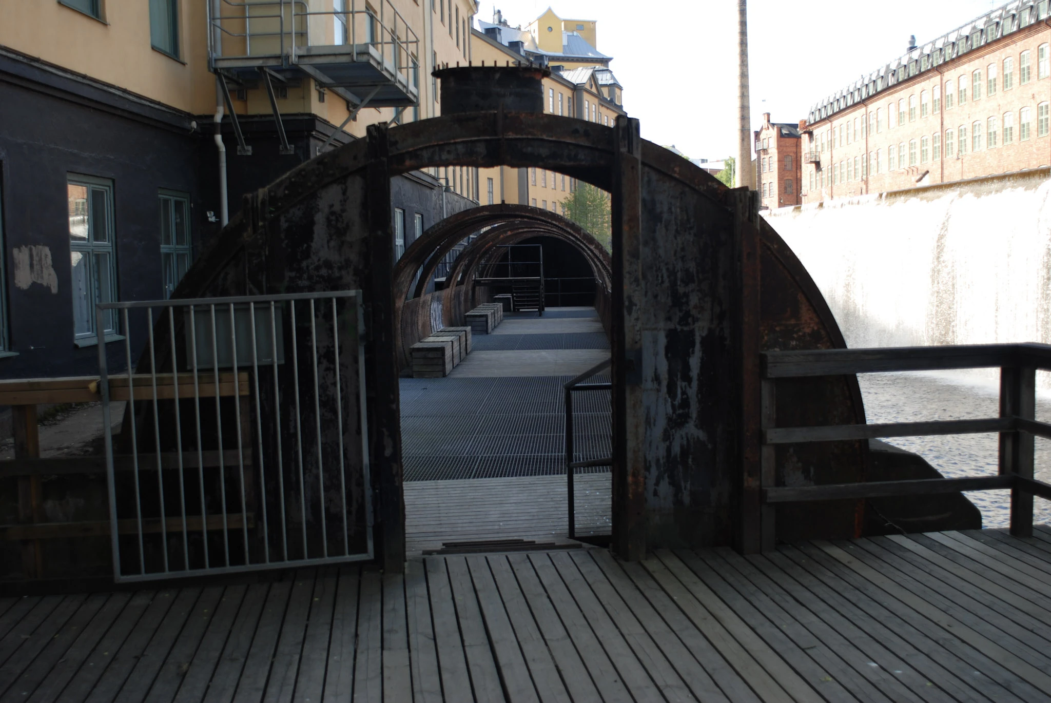 A wooden bridge with a gate in front of two arched bridges between yellow and red buildings.