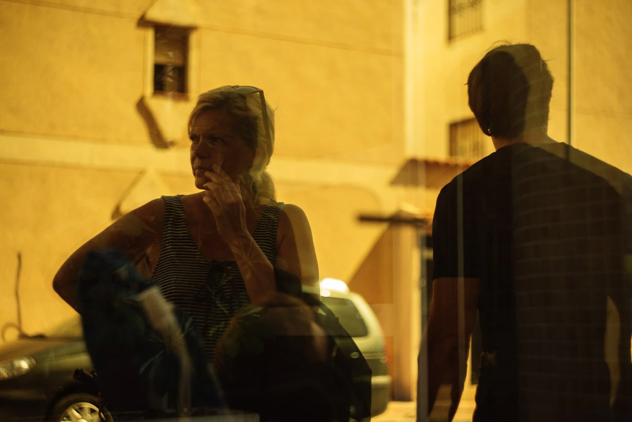 Two people are reflected in a warm yellow-lit pane.
