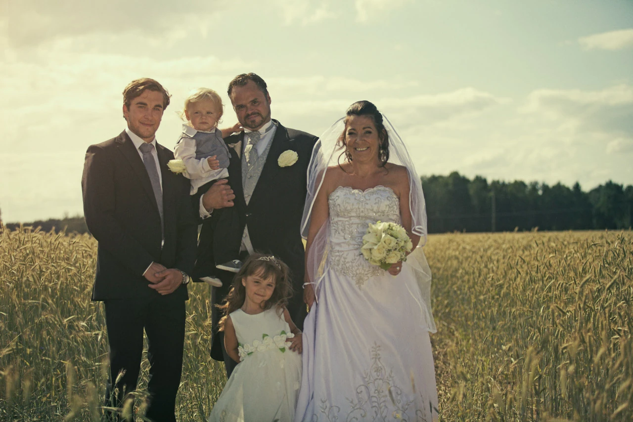 Brudpar och familj samlas för ett porträtt i ett sädesfält.