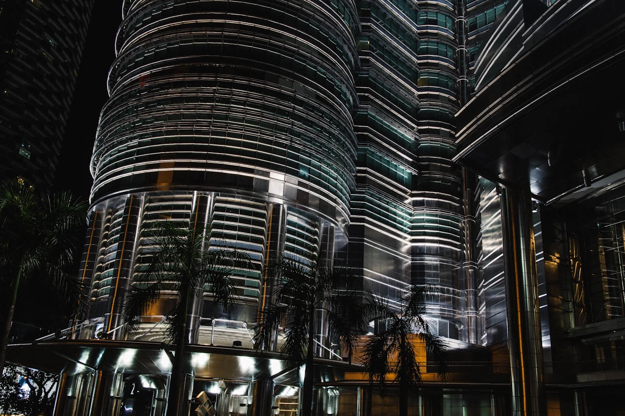 The curved glass and metal facade of an illuminated skyscraper seen from below at night.