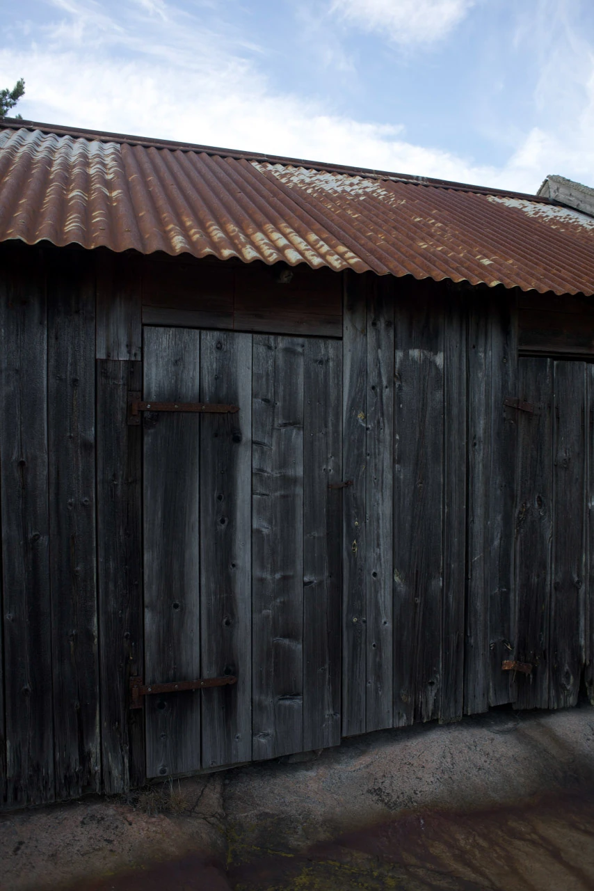 A dark weathered timber wall with a closed door beneath a rust-brown metal roof.
