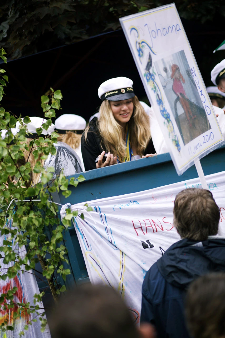 En ung kvinna i studentmössa står på ett dekorerat studentflak.